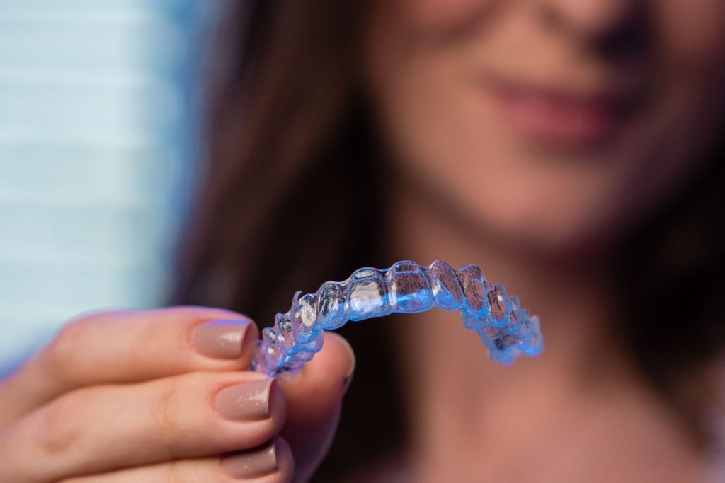 Woman showing a clear Invisalign aligner at a dental clinic